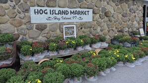 A stone wall with a sign for Hog Island Market, surrounded by potted plants and flowers. - Large Cottage:  Private Beach/Stunning Sunsets/Kayaks/Fire Pit (Swanton)