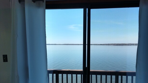 A balcony with a view of a calm lake and distant shoreline. - Large Cottage:  Private Beach/Stunning Sunsets/Kayaks/Fire Pit (Swanton)