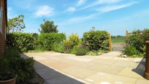 A paved patio with a brick wall on one side and a garden with various plants and flowers. - Rural peace & luxury near Malton, beautiful barn, stunning views, woodburner (Malton)