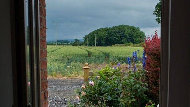 A doorway leading to a garden with a stone pathway, a brick wall, and a view of a green field and trees. - Rural peace & luxury near Malton, beautiful barn, stunning views, woodburner (Malton)