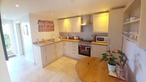 A modern kitchen with white cabinets, a wooden countertop, and a dining table with a potted plant. - Rural peace & luxury near Malton, beautiful barn, stunning views, woodburner (Malton)