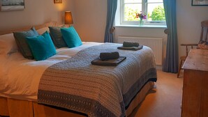 A bedroom with a large bed, a bedside table, a window with curtains, and a radiator. - Rural peace & luxury near Malton, beautiful barn, stunning views, woodburner (Malton)
