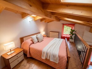 Una camera da letto con soffitto in legno, un letto con copripiumino rosa, comodini, una cassettiera e una finestra con tenda rossa.