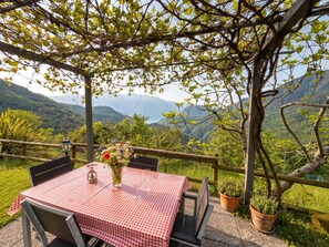 A table set outdoors with a checkered tablecloth, surrounded by chairs, a vase of flowers, and a view of a mountainous landscape.