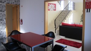 Een moderne woonkamer met een trap, een eethoek met een rode tafel en zwarte stoelen, en een rood tapijt.