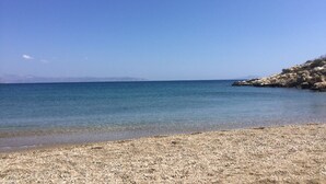 A pebble beach with clear blue water and rocky terrain.
