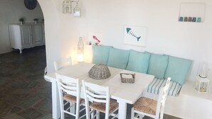A dining area with a white table and chairs, a teal sofa with striped cushions, and a wall-mounted light fixture.