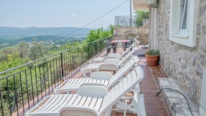 A terrace with white lounge chairs and a table, overlooking a scenic landscape.
