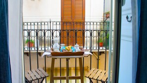 Un balcon avec une table dressée pour deux personnes, sur laquelle se trouve un plateau de nourriture et de boissons, ainsi que deux chaises en bois.