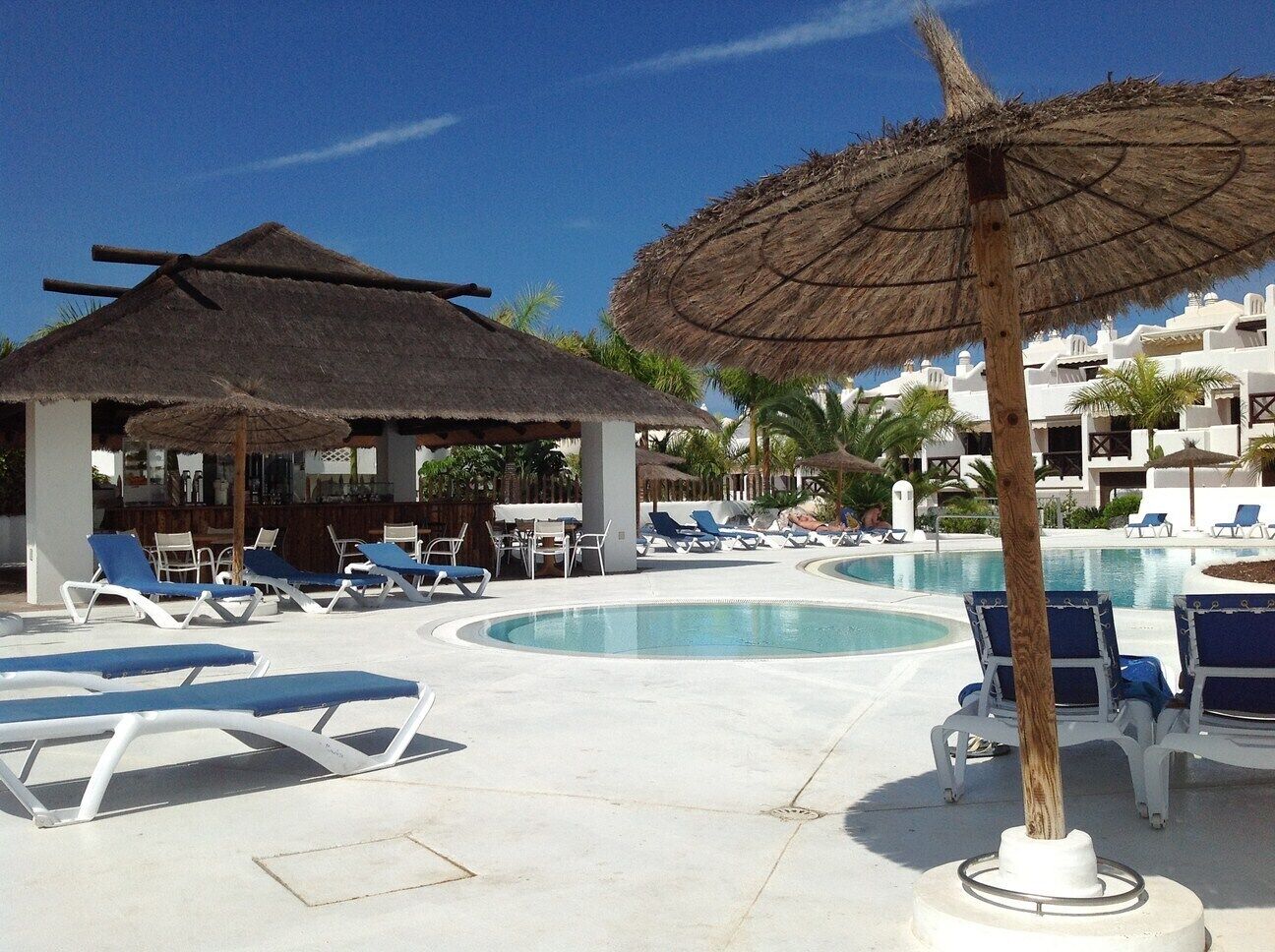 A pool area with lounge chairs, a thatched umbrella, and a pool.
