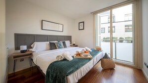 A neatly made bed with a green blanket, a tray of pastries, and a basket of oranges on the bedside table. - Four bedroom apartment Ronda Sant Pere - You Stylish (Barcelona)