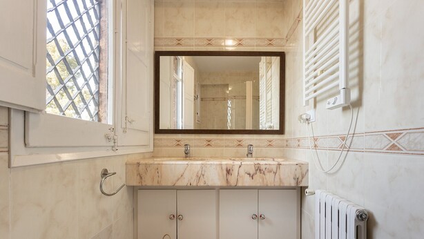A bathroom with a marble sink, a large mirror, a radiator, and a window with a metal grid. - Spacious Luxury Villa with Heated Pool, A/C, Near Barcelona, Vineyards & Golf (Castellví de Rosanes)
