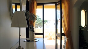Une pièce avec une table, une lampe, une plante en pot et une vue sur l’extérieur, visible à travers une porte vitrée et des rideaux.