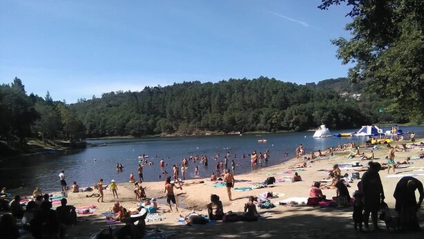 A crowded beach with people sunbathing and swimming, surrounded by trees and a body of water. - Happy group or large family holiday - Free Wifi (Felgueiras)