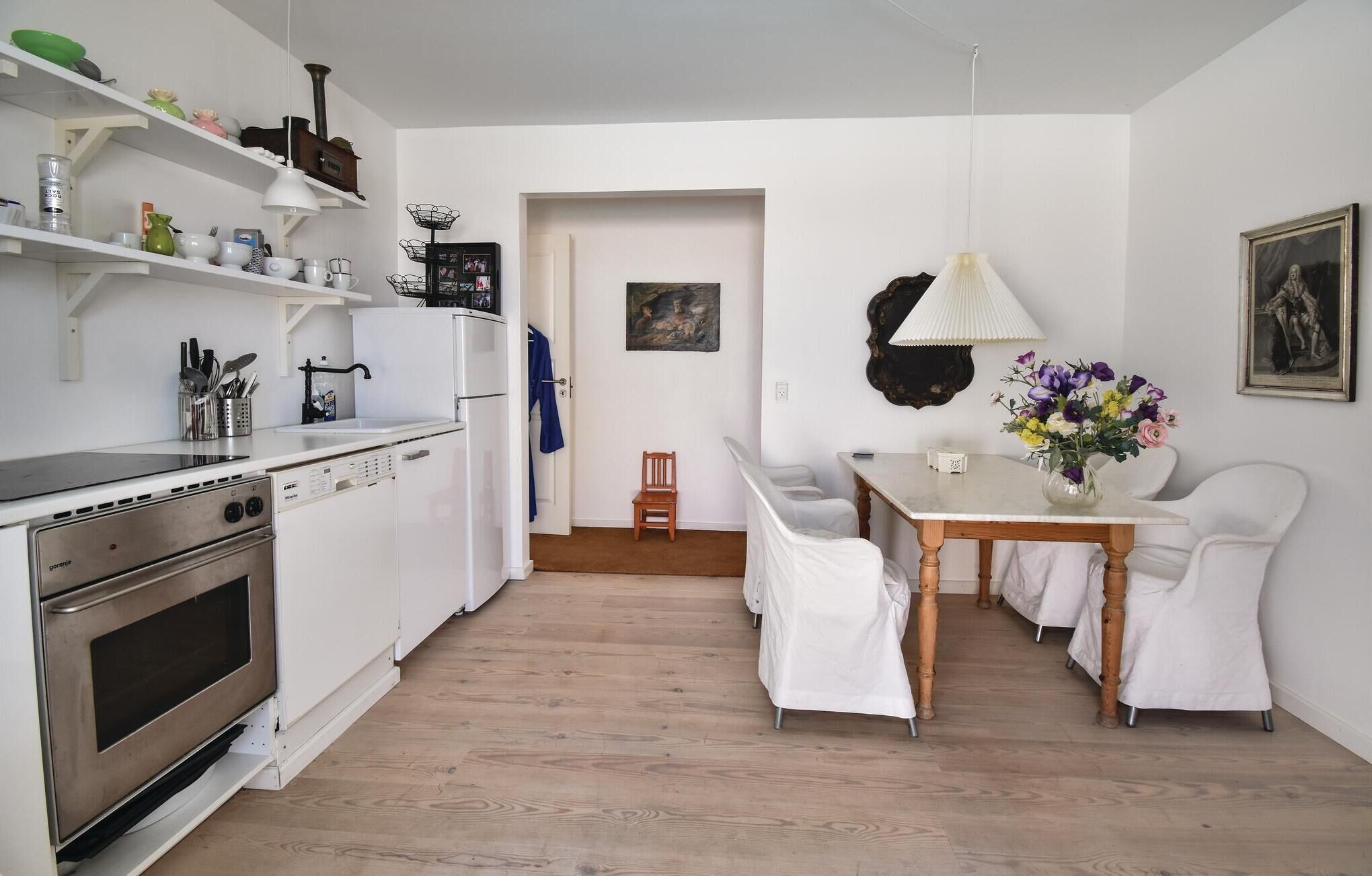 A compact kitchen with white appliances, a dining area with a table and chairs, and a hallway leading to another room.