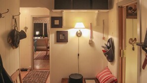 Un couloir avec une lampe, une porte ornée d’un motif de coq et une petite table sur laquelle repose un coussin rouge.