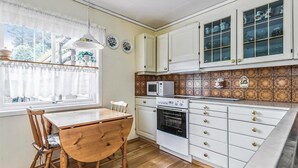Une cuisine compacte avec des meubles blancs, un four à micro-ondes, un four traditionnel et une table à manger avec des chaises.