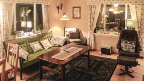 Un salon chaleureux avec un canapé vert, une table basse en bois, un fauteuil en cuir et un tapis à motifs.