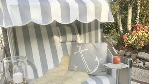 Ein gestreifter Gartenstuhl mit einer flauschigen Decke, einem Glaslaternenfuß und einem Tablett mit einem Apfel.