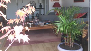 A living room with a sofa, a coffee table with books, a potted plant, and a painting on the wall.