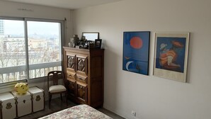 A bedroom with a bed, a dresser, a chair, a suitcase, and two framed artworks on the wall.