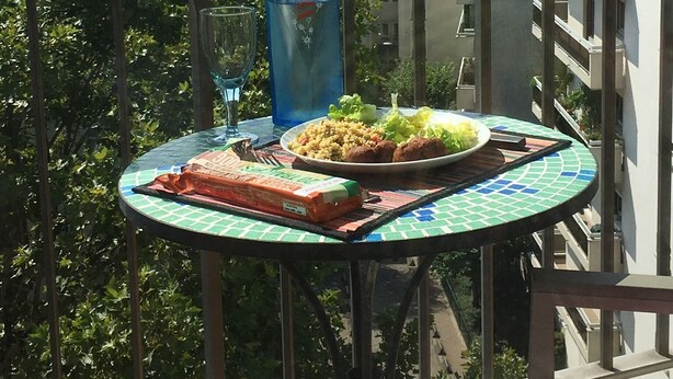 A balcony with a table set for a meal, a bottle of water, and a glass of wine.