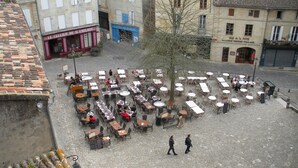 Un café en plein air avec des tables et des chaises disposées en cercle, entouré de bâtiments dont les devantures sont bien visibles.