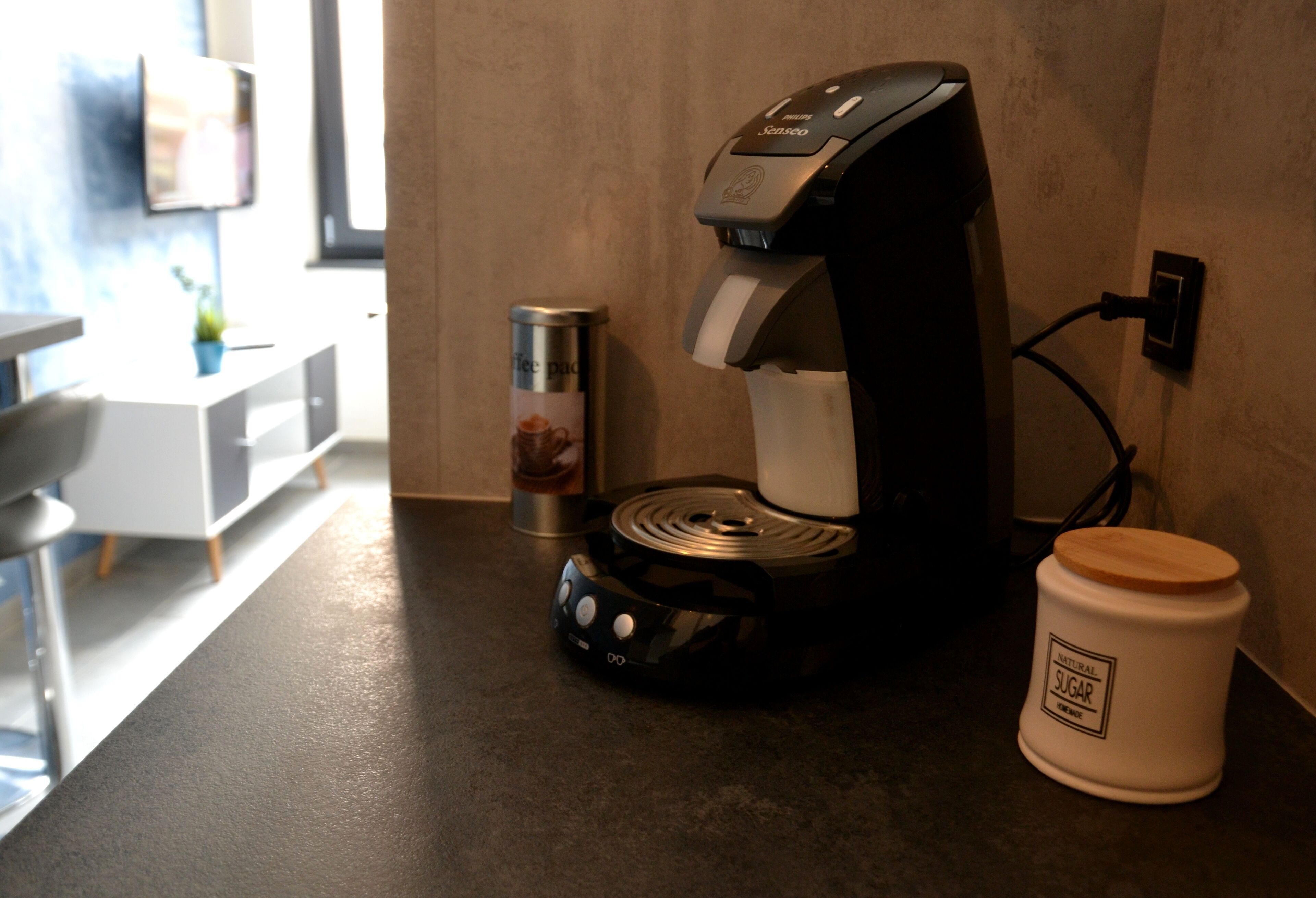 Une machine à café, un récipient et un sucrier sont posés sur le plan de travail de la cuisine.