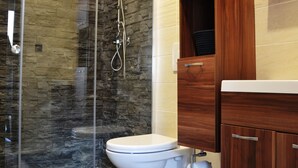 Un baño moderno con cabina de ducha de vidrio, inodoro blanco y muebles de madera.