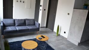 Una sala de estar moderna con un sofá gris, dos mesas redondas de madera y un tapete azul oscuro.