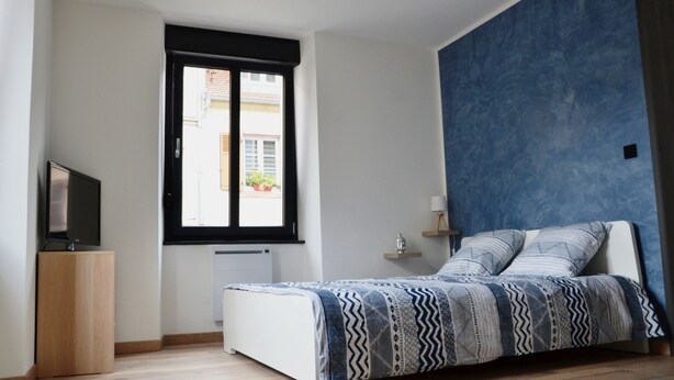 Un dormitorio con una cama, un televisor sobre un mueble de madera, una ventana con vistas al exterior y una pared de acento azul.