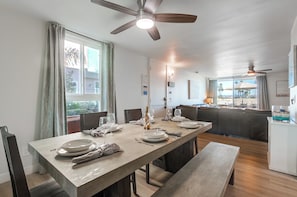 Un comedor con una mesa larga dispuesta para cuatro, un ventilador de techo y vistas al área de estar exterior.
