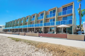 Un hotel moderno con varios balcones, mobiliario exterior y ubicación frente a la playa.