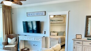 Un salón con televisor, sofá, sillón de mimbre, ventilador de techo y un cartel que dice 'Beach House'.