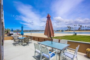 An outdoor patio with a table and chairs, a grill, and a view of the beach and ocean. - Enjoy the breeze at this beautiful bayfront condo! (San Diego)