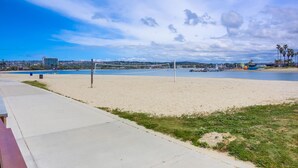 Una cancha de voleibol de playa con red, zona arenosa y una masa de agua al fondo.