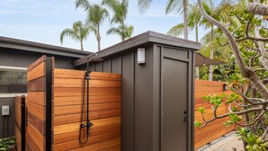 A modern outdoor shower area with a wooden enclosure and a metal door, surrounded by lush greenery.