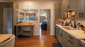 A modern kitchen with grey cabinets, a stainless steel refrigerator, a wooden dining table, and a built-in sink.