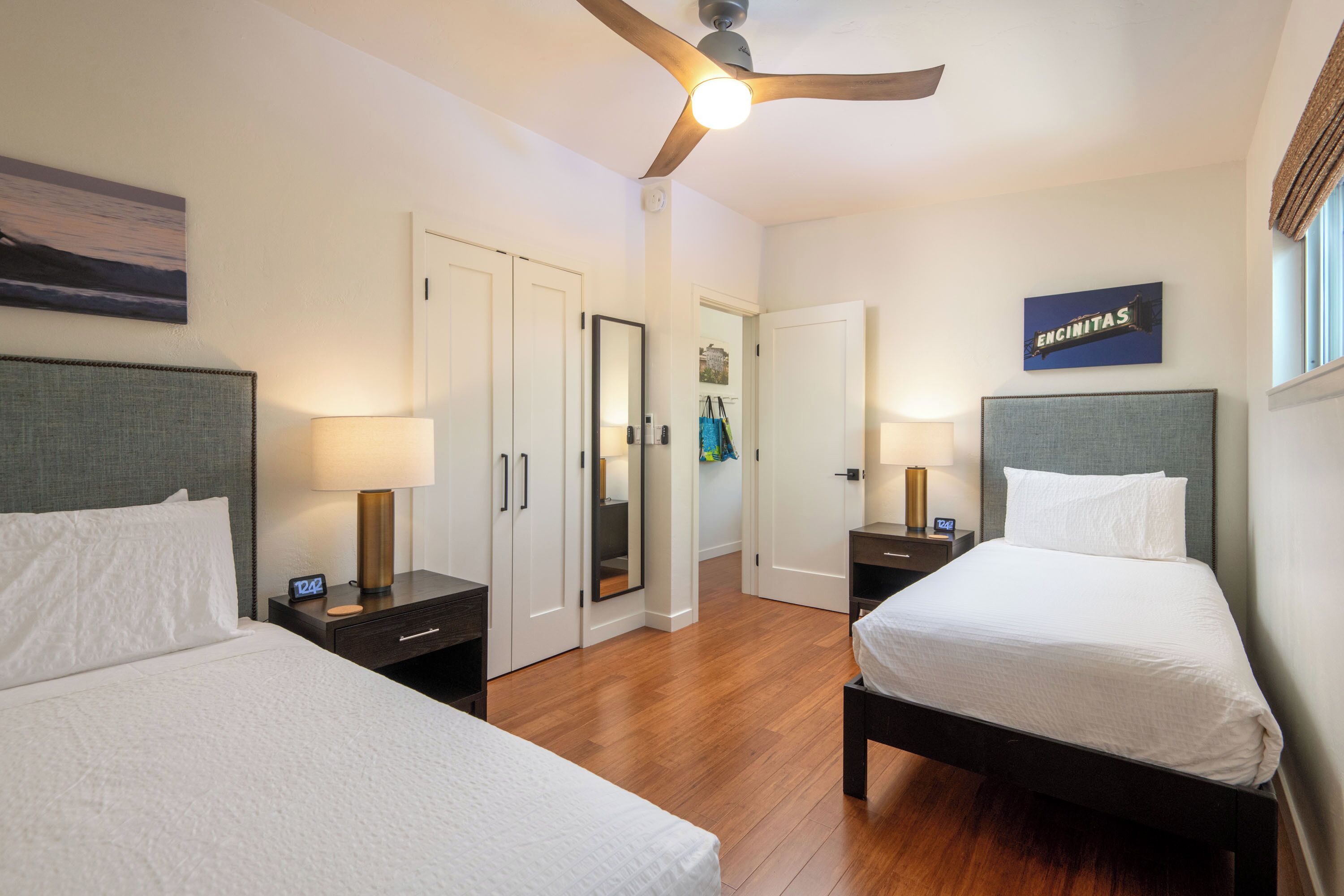 A hotel room with two beds, wooden flooring, a ceiling fan, and a wall-mounted sign.