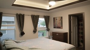 A bedroom with a bed, a dresser, a painting, and a window with curtains.
