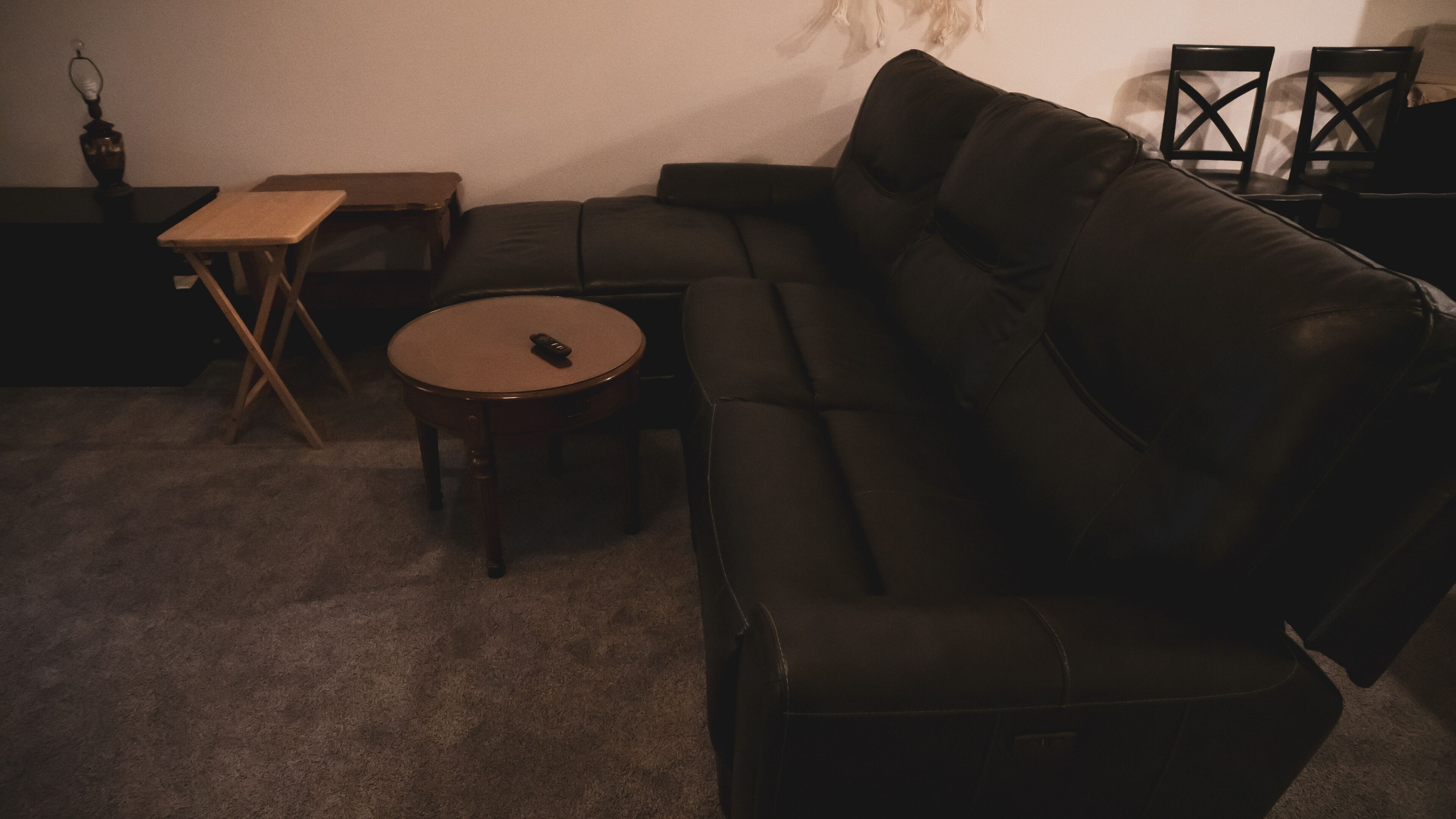 Un salon avec un canapé en cuir noir, une petite table en bois et une télécommande posée sur la table.