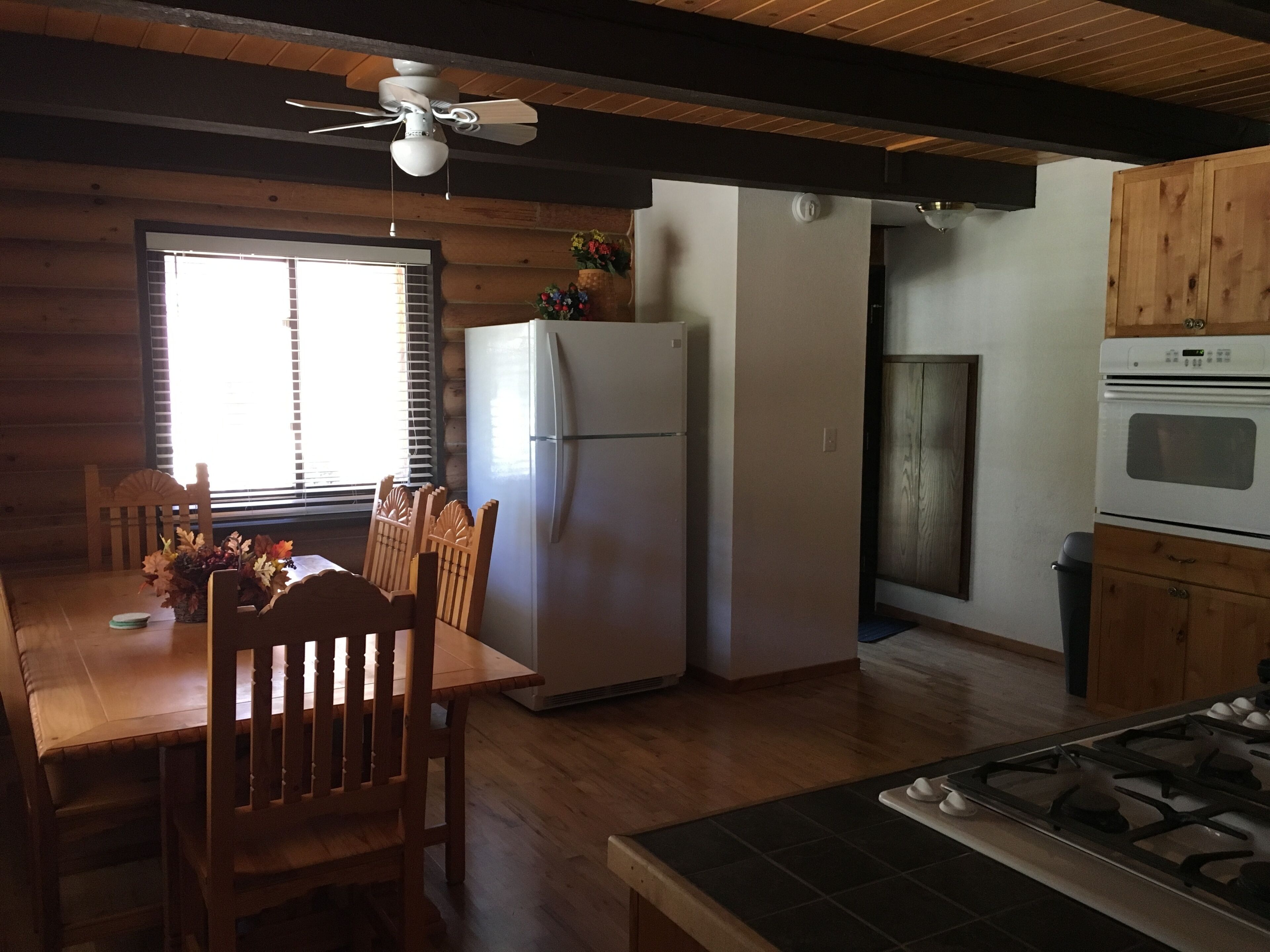 A kitchen with wooden cabinets, a refrigerator, a stove, and a dining area with a table and chairs.