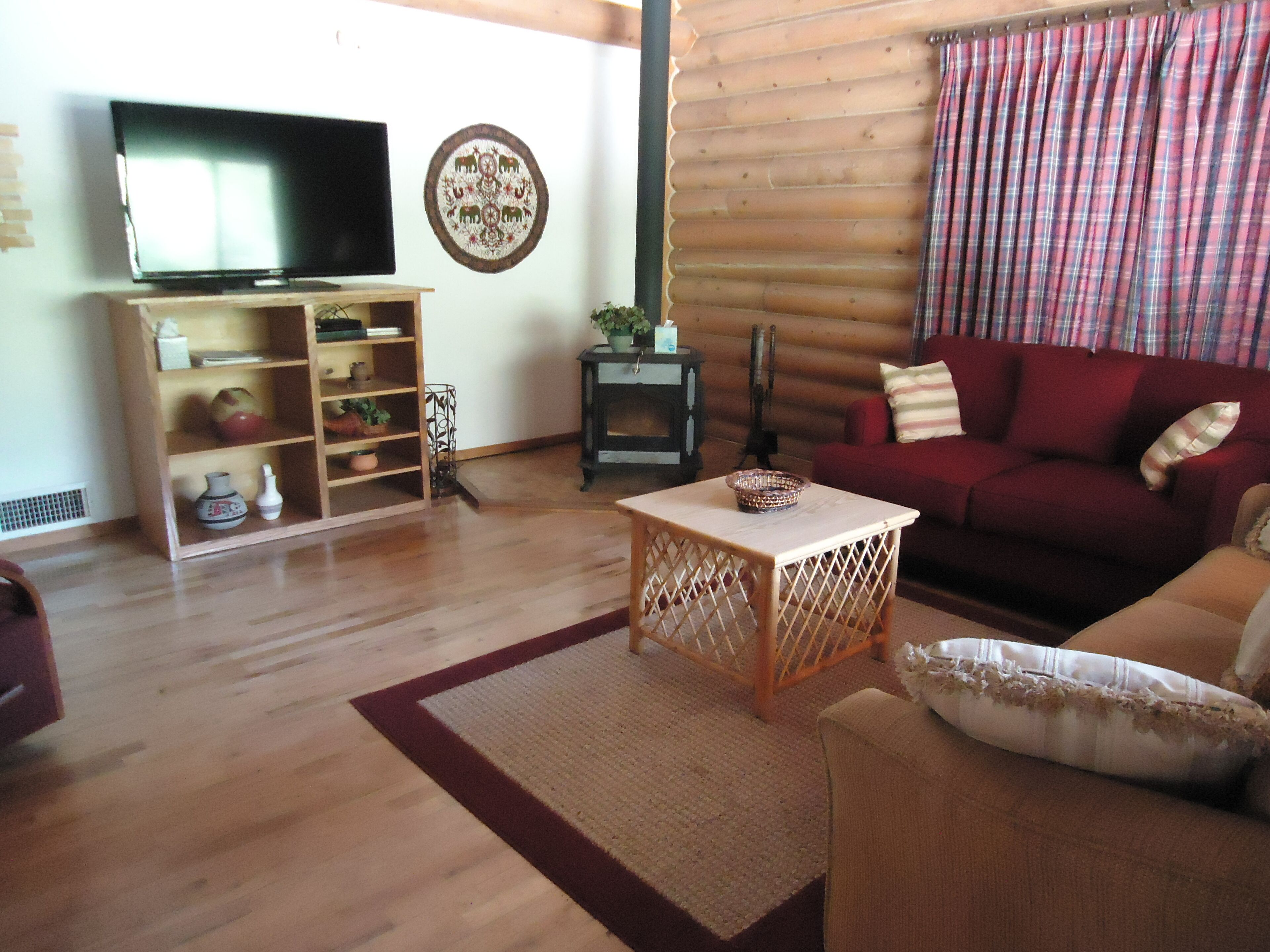 Una sala de estar acogedora con piso de madera, televisor, estantería, chimenea y sofá rojo.