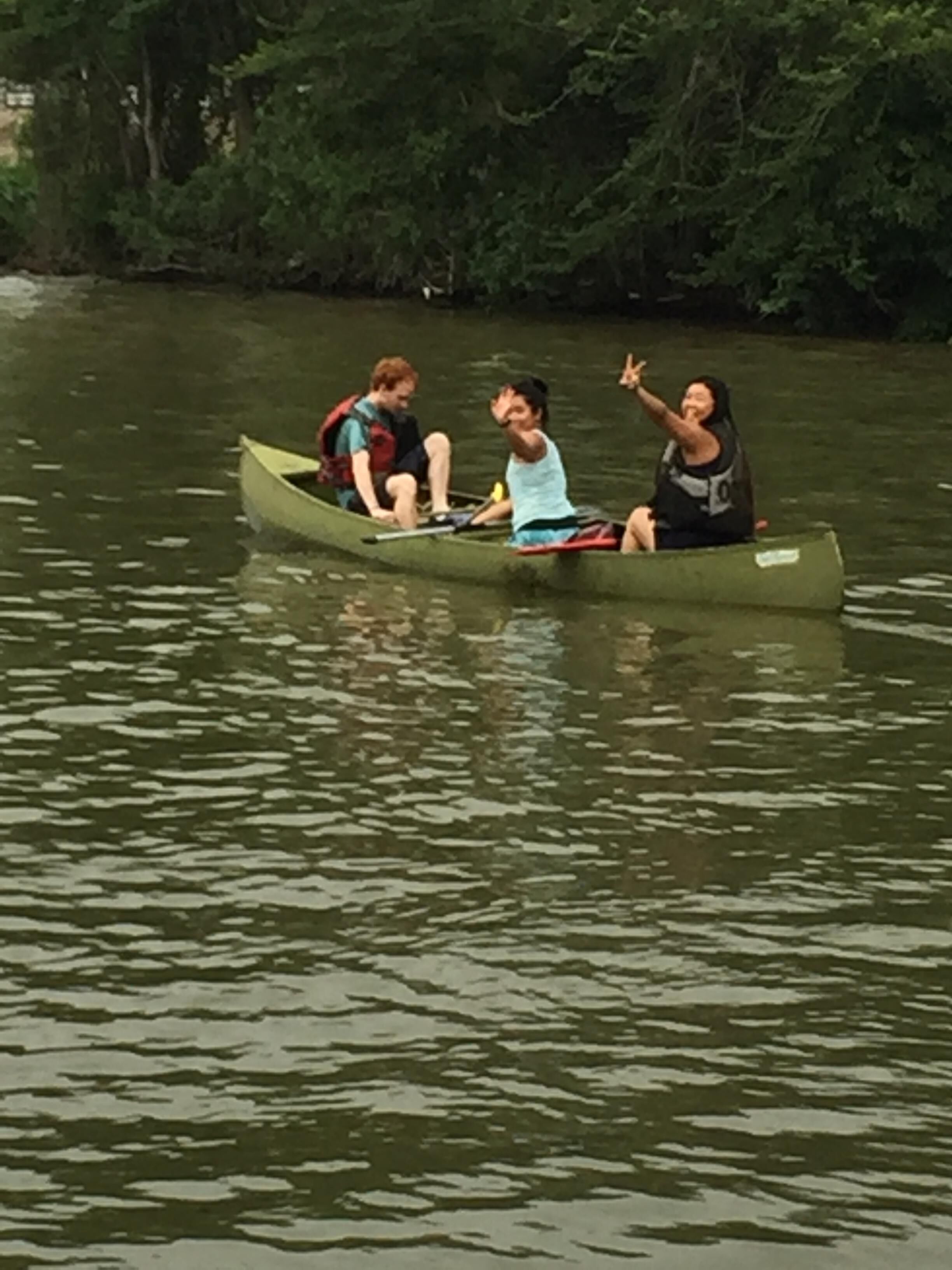 Uma canoa verde pequena em águas calmas, com três pessoas usando coletes salva-vidas.