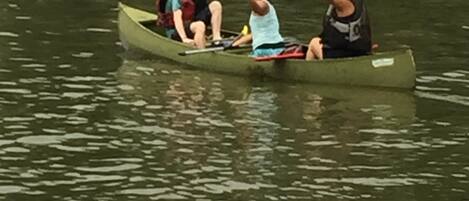 Uma canoa verde pequena em águas calmas, com três pessoas usando coletes salva-vidas.