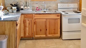A kitchen with wooden cabinets, a white stove, a microwave, and a window with a floral curtain.