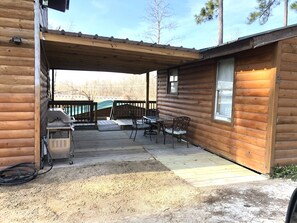 Ein überdachter Patio-Bereich mit Tisch, Stühlen, einem Grill und einer Holzterrasse.