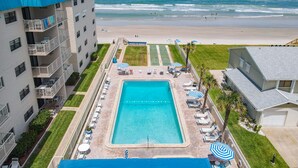 A hotel with a swimming pool, beach view, and a tennis court.