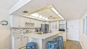 A modern kitchen with white cabinets, a large island with stools, a ceiling fan, and a backsplash with a geometric pattern.