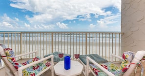 A balcony with a view of the beach, featuring a table with two wine glasses and a blue candle.
